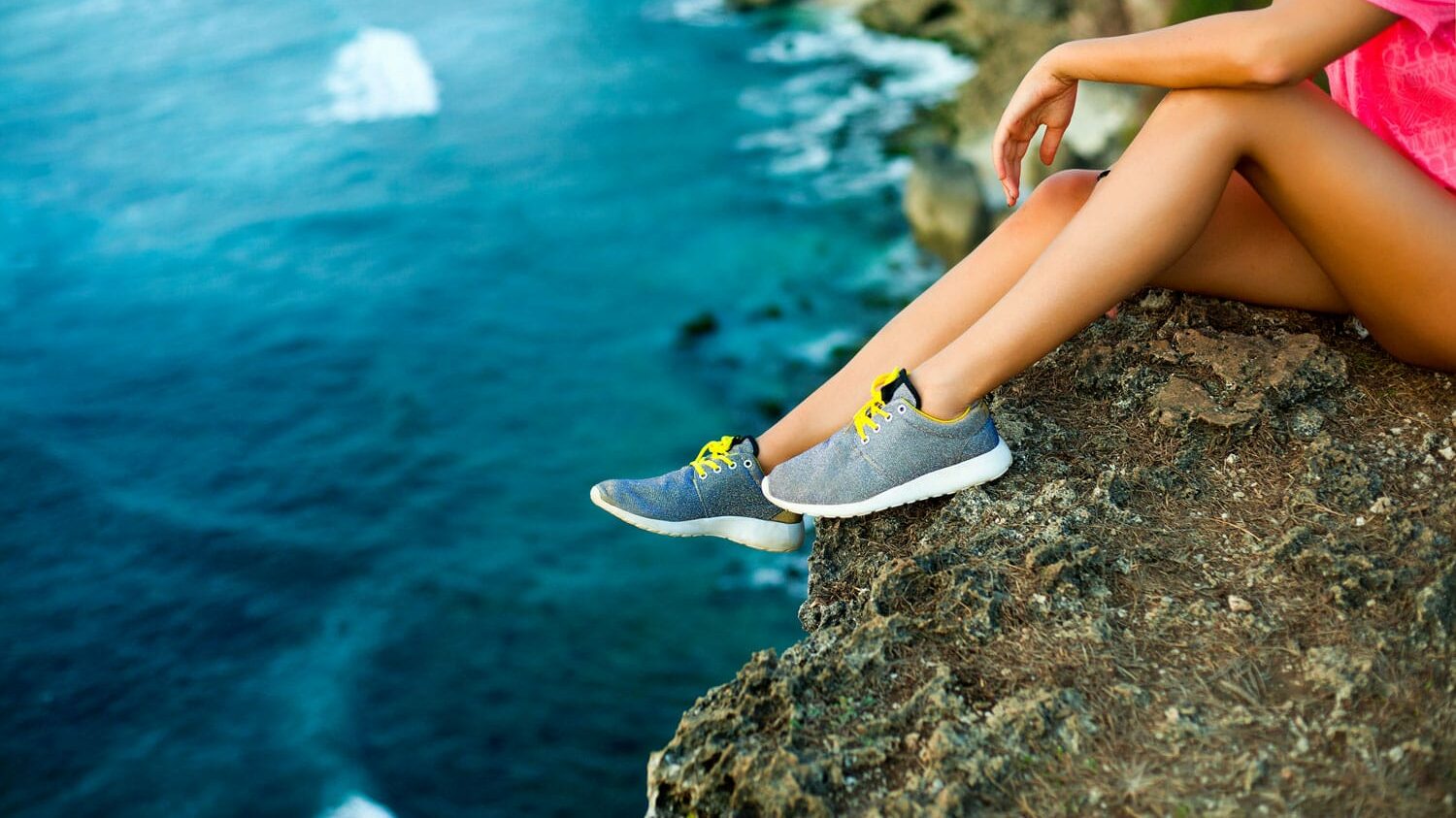 Girl on vacation sitting on a cliff with her shoes 